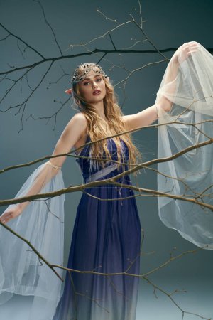 Una joven con un vestido azul se levanta con gracia frente a un árbol imponente, encarnando a una princesa de hadas etérea en un entorno de estudio.