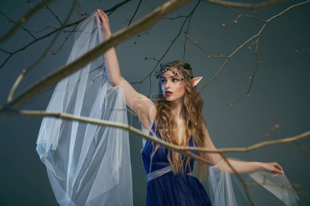 Eine junge Frau in einem blauen Kleid hält anmutig einen zarten weißen Schleier in einem zauberhaften Studio, das für eine Elfenprinzessin geeignet ist.
