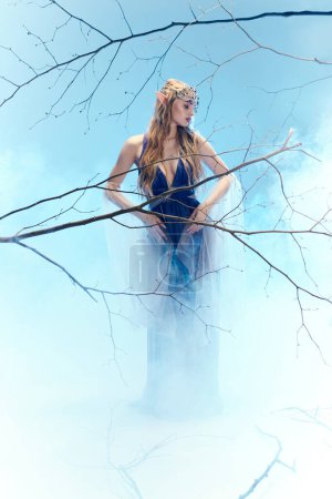 Una joven vestida como una princesa elfa se levanta con gracia en la niebla.