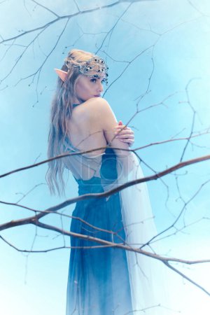 Une jeune femme en robe bleue, ressemblant à une princesse elfe, se tient gracieusement devant un arbre majestueux.