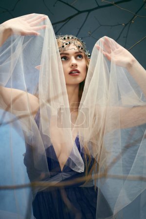 Eine junge Frau verkörpert ein Märchen, als sie in einem Atelier in einem atemberaubenden blauen Kleid mit Schleier über dem Kopf steht.