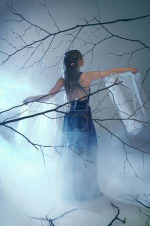 A young woman in a blue dress stands in a foggy forest, embodying a fairy tale character or elf princess.