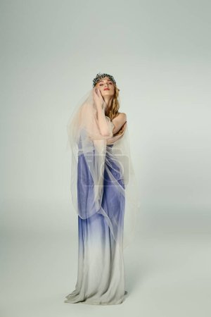 Eine junge Frau in einem blau-weißen Kleid mit einem fließenden Schleier, die das Wesen einer Märchenprinzessin in einem Atelier verkörpert.