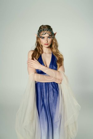 Eine junge Frau strahlt Eleganz in einem blauen Kleid mit einem zarten Schleier aus und verkörpert die Persönlichkeit einer bezaubernden Elfenprinzessin in einem Studio-Setting.