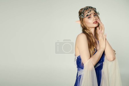 A young woman embodies an elf princess in a blue dress with a delicate veil in a whimsical studio setting.