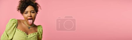 Foto de Elegante mujer afroamericana sobresaliendo lengua sobre fondo rosa. - Imagen libre de derechos