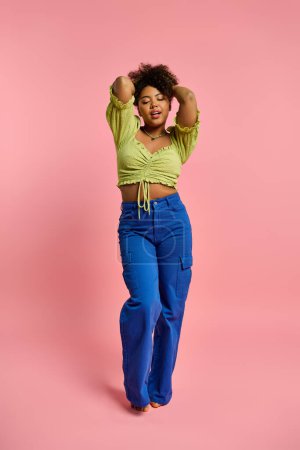 Stylish African American woman poses in yellow top and blue pants against vibrant backdrop.
