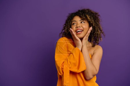 Photo for A beautiful African American woman wearing an orange shirt poses stylishly against a vibrant backdrop. - Royalty Free Image