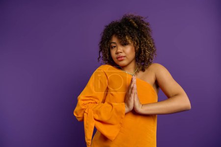 Photo for Stylish African American woman posing in orange top against vibrant purple backdrop. - Royalty Free Image
