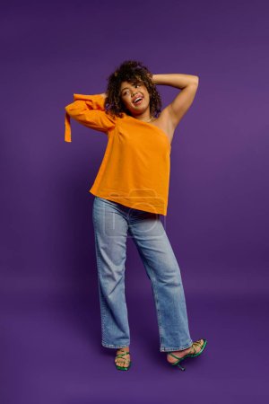 Téléchargez les photos : Femme afro-américaine élégante pose sur fond vibrant en chemise orange. - en image libre de droit