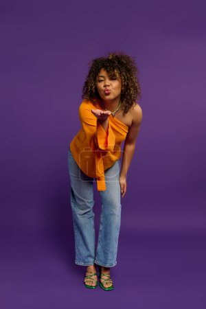 Femme afro-américaine élégante frappant une pose sur un fond violet vibrant.