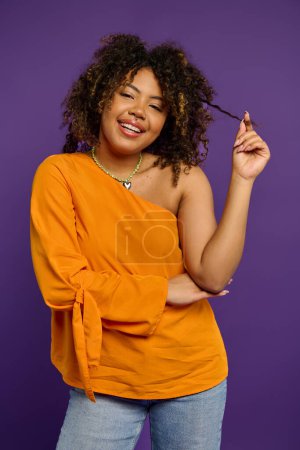 Foto de Elegante mujer afroamericana en top naranja tocando su cabello. - Imagen libre de derechos
