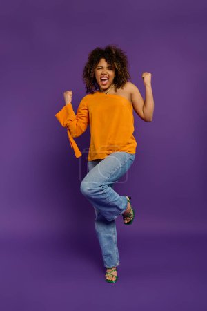 Photo for Stylish African American woman in orange top dances with emotion. - Royalty Free Image