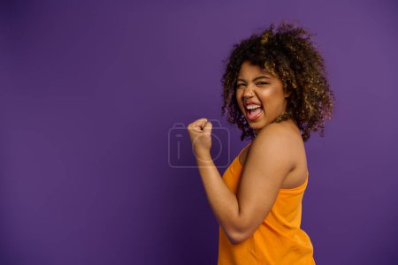 Una mujer afroamericana con estilo en una camiseta naranja golpea una pose contra un vibrante telón de fondo.