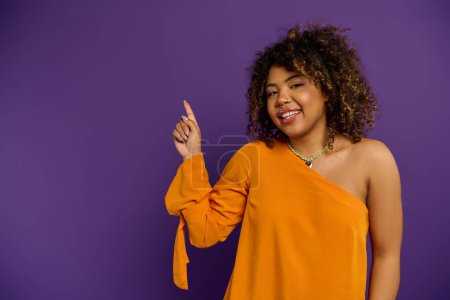 Téléchargez les photos : Une belle femme afro-américaine en robe orange pose gracieusement sur un fond vibrant. - en image libre de droit