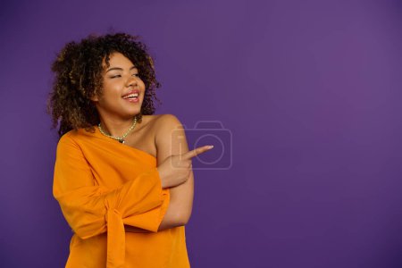 Une femme afro-américaine en tenue élégante pointe avec confiance quelque chose.