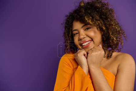 Foto de Hermosa mujer afroamericana con el pelo rizado que golpea una pose en traje elegante contra un telón de fondo vibrante. - Imagen libre de derechos