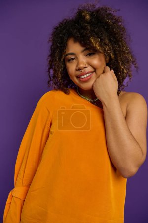 Téléchargez les photos : Femme afro-américaine élégante posant dans une chemise orange sur un fond vibrant. - en image libre de droit