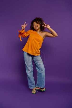 Photo for African American woman in stylish attire posing with peace sign against vibrant backdrop. - Royalty Free Image