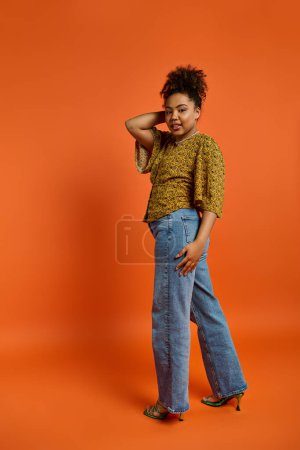 Foto de Hermosa mujer afroamericana en traje elegante golpeando una pose contra un fondo naranja vibrante. - Imagen libre de derechos
