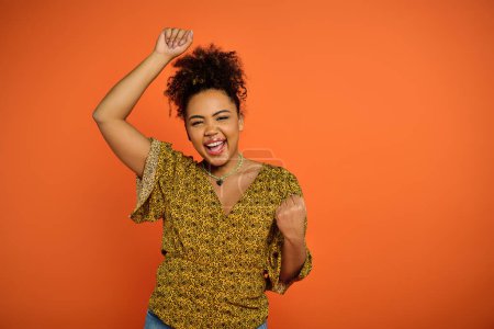 Photo for Beautiful African American woman in stylish attire joyfully raises her arms in the air against a vibrant backdrop. - Royalty Free Image