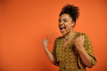 Foto de Una hermosa mujer afroamericana con la boca abierta posando sobre un vibrante telón de fondo naranja. - Imagen libre de derechos