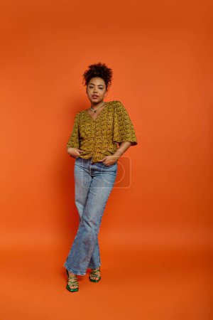 Téléchargez les photos : Une femme afro-américaine élégante pose en toute confiance devant une toile de fond orange vibrante. - en image libre de droit