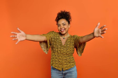 A stylish African American woman with arms outstretched against a vibrant orange backdrop.