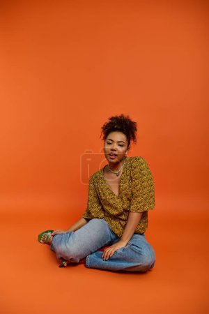 Photo for African American woman in stylish attire, sitting cross-legged on vibrant floor. - Royalty Free Image