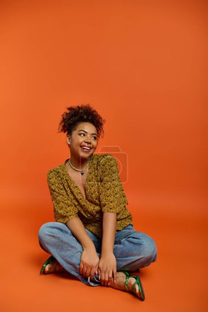 Téléchargez les photos : Une femme afro-américaine en tenue élégante s'assoit gracieusement avec les jambes croisées. - en image libre de droit