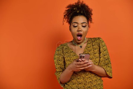 Téléchargez les photos : Femme afro-américaine en tenue élégante tenant le téléphone portable, faisant drôle visage. - en image libre de droit