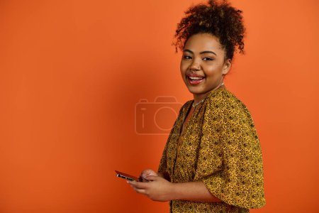 A beautiful African American woman in a yellow dress poses with a cell phone.