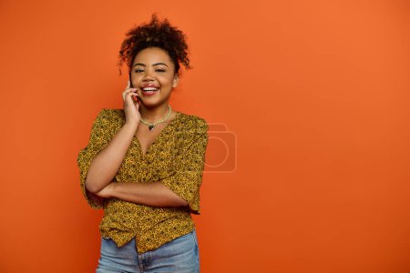 Femme afro-américaine souriante en tenue élégante parlant sur un téléphone portable sur fond vibrant.