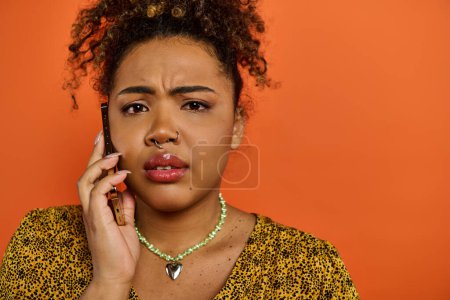Foto de Mujer afroamericana con un atuendo elegante, sosteniendo un teléfono celular en su oído. - Imagen libre de derechos