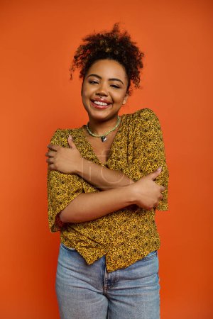 Photo for Stylish African American woman with crossed arms against vibrant orange backdrop. - Royalty Free Image