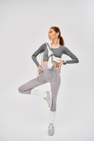 A sporty young woman wearing gray and white activewear poses on a grey background.