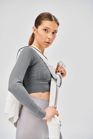 Une jeune femme sportive en soutien-gorge de sport et leggings, dégage énergie et confiance sur fond gris.