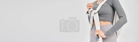 Téléchargez les photos : Une jeune femme sportive exhibant ses vêtements de sport avec confiance sur un fond gris. - en image libre de droit