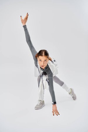 A sporty young woman in active wear dancing gracefully in a studio on a grey background.