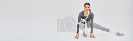 A sporty young woman in active wear stretches her body with grace and strength on a white background.