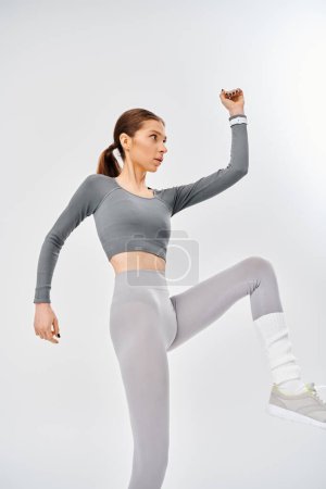 Téléchargez les photos : Une jeune femme sportive dans un haut gris et leggings gris pose gracieusement sur un fond gris apaisant. - en image libre de droit