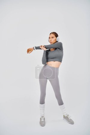 Eine sportliche junge Frau in grauem Top und Leggins trainiert anmutig