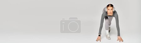 Foto de Deportiva joven con elegancia realiza un soporte de mano en un elegante traje gris sobre un fondo neutro. - Imagen libre de derechos