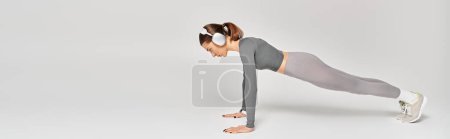 Une jeune femme sportive en tenue active qui fait preuve de force en poussant une jambe sur un fond gris.