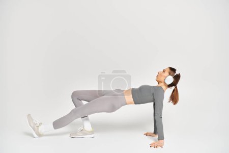 Foto de Una joven deportista realiza un ejercicio de tablón lateral con gracia y fuerza sobre un fondo blanco. - Imagen libre de derechos