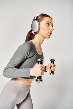 Sportliche Frau in aktiver Kleidung hält Kurzhanteln mit aufgesetzten Kopfhörern bereit für eine Trainingseinheit.