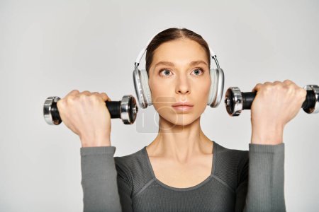 A sporty young woman in active wear wearing headphones, holding two dumbbells.