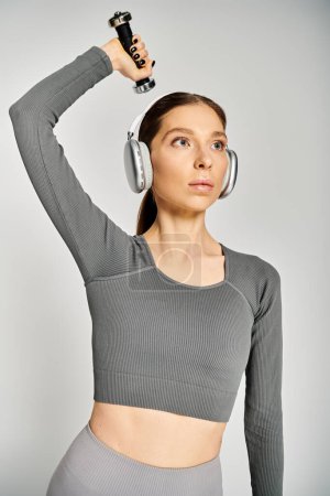 A sporty young woman in active wear, holding a dumbbell and wearing headphones.