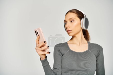 A sporty young woman in active wear listens to music on headphones while holding a cell phone.