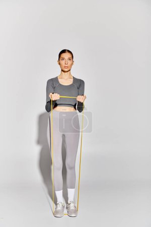 Photo for A sporty young woman in active wear working out with elastics against a grey background. - Royalty Free Image